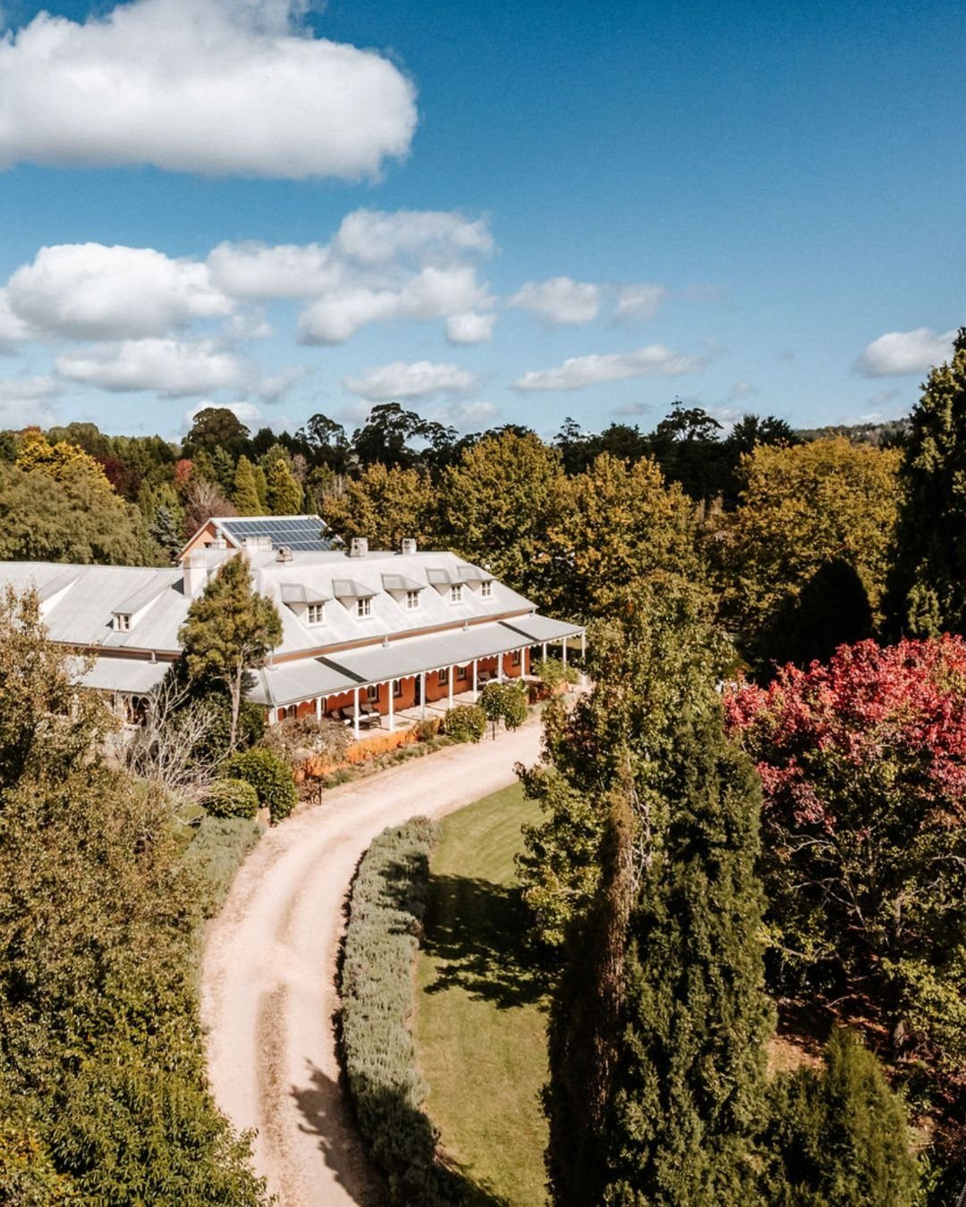 The inn and its gardens from the air, the gravel drive curving up through the trees