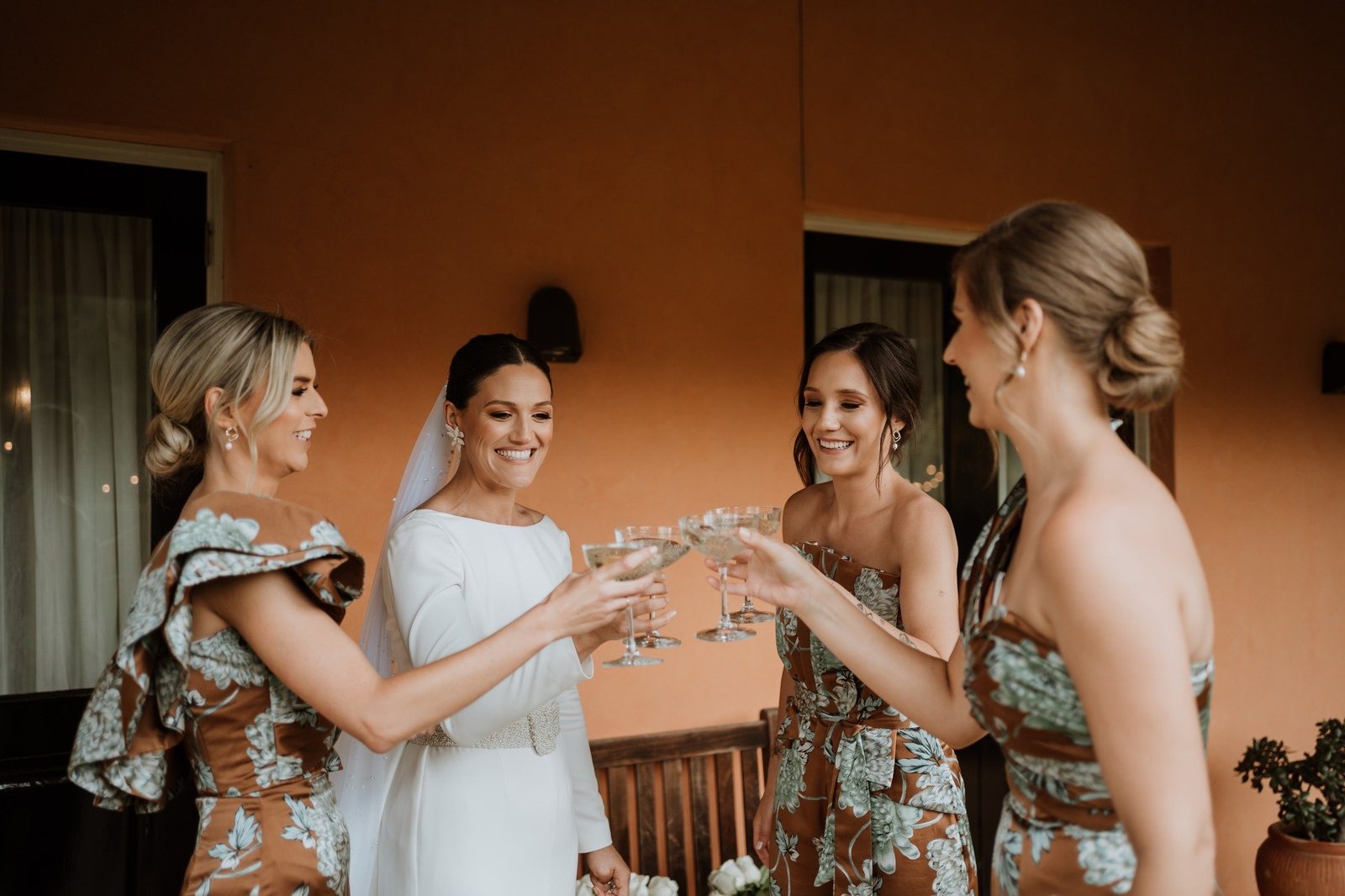 A bride and three bridesmaids clinking glasses on the terracotta verandah