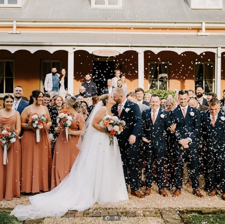 The wedding party in terracotta and navy cheering under confetti in front of the verandah