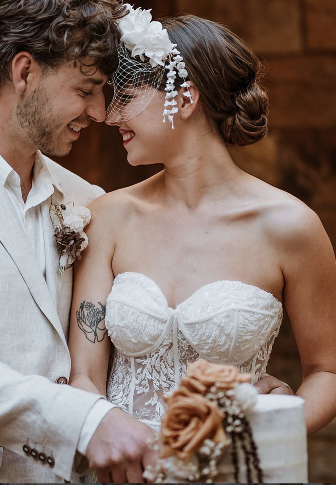 A bride and groom in a cream suit touching foreheads, smiling