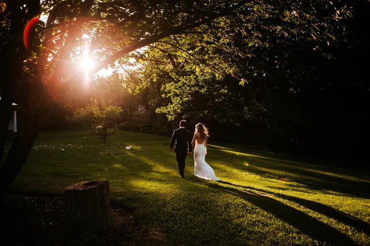 A couple walking across the lawn at golden hour, sun flaring through the trees