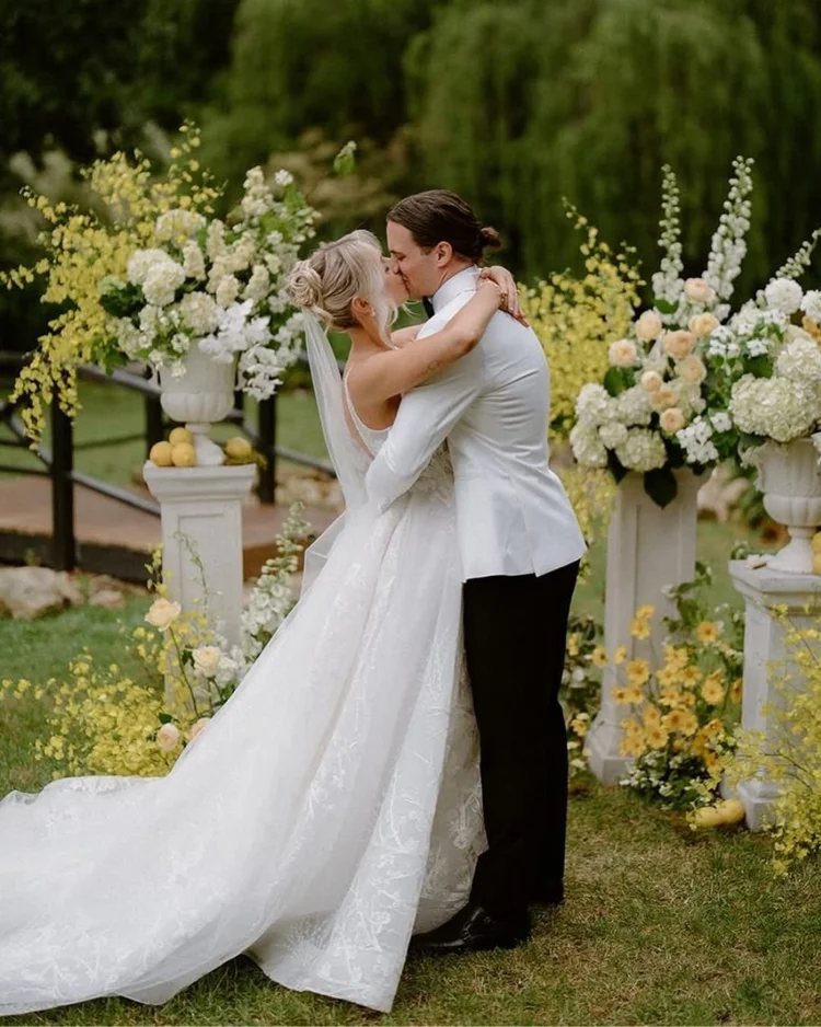 A couple kissing in the garden between tall white floral arrangements